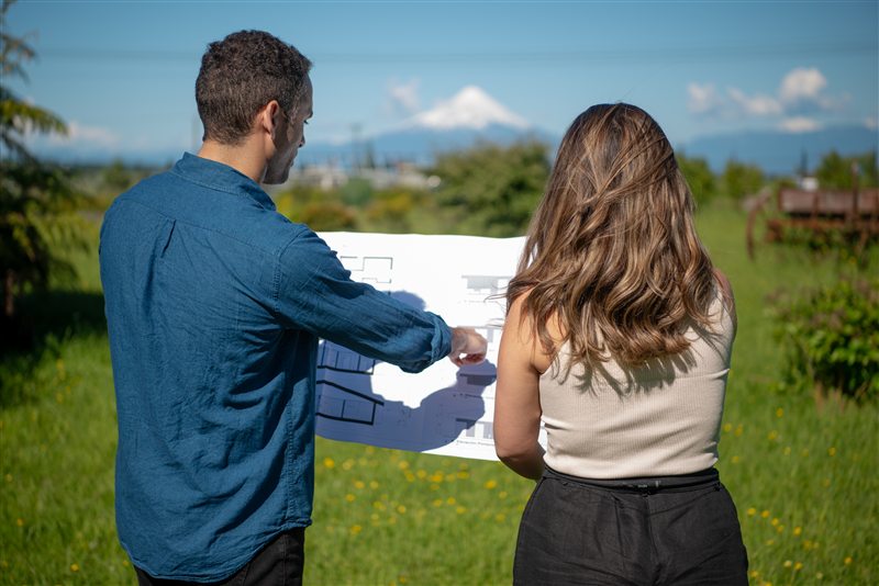 Pareja revisando un plano de terreno con volcán al fondo